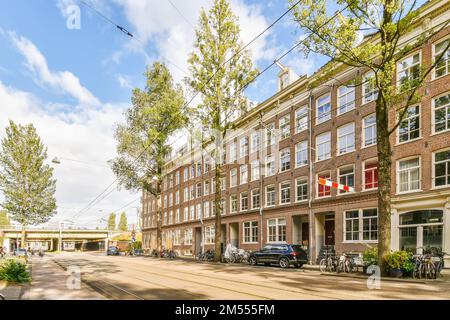 Eine Straße in der Stadt mit Autos, die auf beiden Seiten geparkt sind, und Bäumen, die die Straße säumen, alle aneinander ausgerichtet Stockfoto