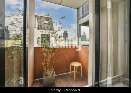 Ein Balkon mit Stuhl und Topfpflanzen auf dem Boden, vor einem offenen Fenster mit Blick nach draußen Stockfoto