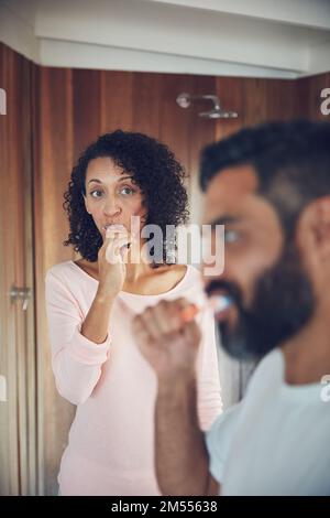 Gibt es etwas, das er mir nicht sagt? Eine reife Frau, die ihren Mann ansieht, während sie sich im Bad die Zähne putzt. Stockfoto