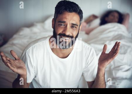 War es etwas, das ich in ihrem Traum sagte? Porträt eines erwachsenen Mannes, der verwirrt aussieht, während seine Frau im Hintergrund schläft. Stockfoto