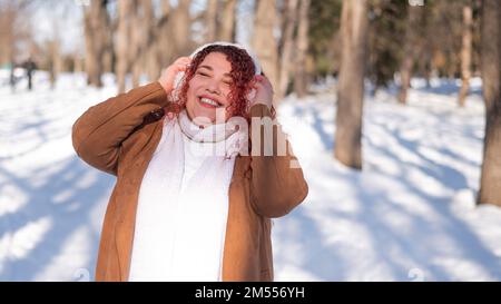Fröhliche fette kaukasische Frau in Pelzkopfhörern im Freien. Stockfoto