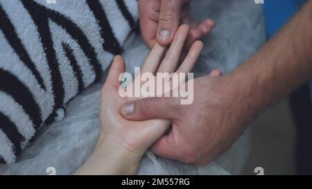 Ein Masseur massiert die Handgelenke eines Mädchens. Stockfoto