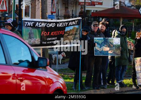 Tenterden, Kent, Großbritannien. 26. Dezember 2022. Das jährliche Treffen am zweiten Weihnachtsfeiertag der Ashford Valley Tickham Hunt findet an einem hellen und sonnigen, aber kalten Morgen in der Stadt Tenterden, Kent, statt. Pferde und Hunde versammeln sich um 11am Uhr im Pub „The Vine Inn“, bevor es die Hauptstraße hinunter zu einem vollgepackten Publikum geht. Demonstranten zeigen ihre Banner beim vorbeifahrenden Verkehr. Foto: Paul Lawrenson/Alamy Live News Stockfoto