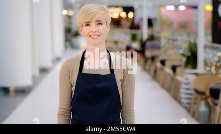 Porträt weibliche Mitarbeiterin im Café. Reife, 40s-köpfige Erwachsene Frau mittleren Alters, die ziemlich lächelnde Kellnerin, Restaurantbesitzerin, Verkäuferin im Einkaufszentrum Stockfoto