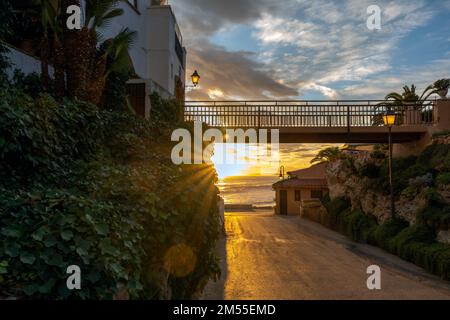 Gerade Asphaltstraße unter der Fußgängerbrücke vor dem Hotel in der Nähe des winkenden Meeres am bewölkten Abend des Resorts Stockfoto