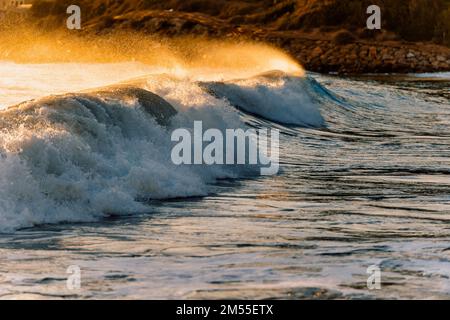 Schäumende Wellen von sauberem Meer, das im Sommer bei Sonnenuntergang in der Nähe der Küste rollt und spritzt Stockfoto