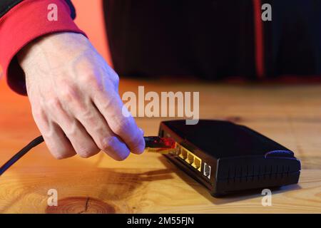 Person im Hintergrund, die das Internetkabel in das alte adsl-Modem einsteckt Stockfoto