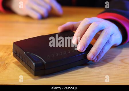 Schwarzes adsl-Modem auf dem Tisch mit einer Hand und einer verschwommenen Person im Hintergrund Stockfoto