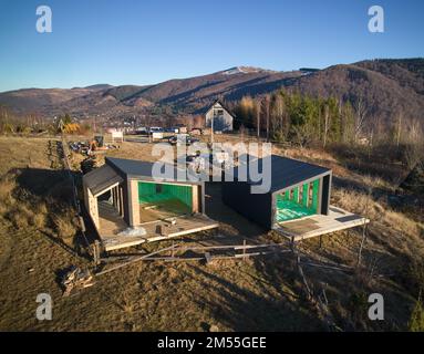 Luftaufnahme von zwei Holzrahmenhäusern im skandinavischen Stil, die mit Polyurethanschaum isoliert sind. Bau- und Isolierkonzept. Stockfoto