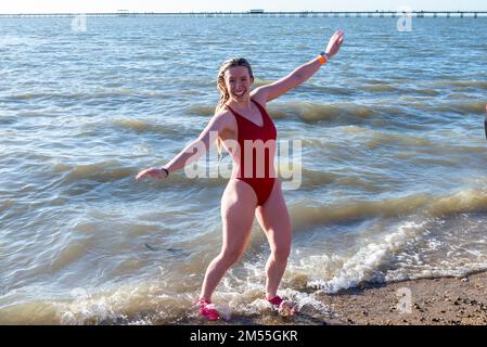 Jubilee Beach, Marine Parade, Southend on Sea, Essex, Großbritannien. 26. Dezember 2022. Wie es Tradition an Orten am Meer geworden ist, fand ein „Boxing Day Dip“ in der kalten, rauen Themsenmündung in Southend on Sea in der Nähe des Stadtpiers statt und sammelte Gelder für die örtliche Royal National Lifeboat Institution. Etwa 400 Personen gingen zum Wasser, das etwa 6 Grad Celsius betrug. Eine Schwimmerin in rotem Badeanzug, die das Meer verlässt Stockfoto