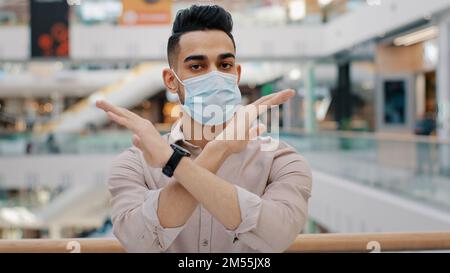 Indischer hispanischer Mann in medizinischer Gesichtsmaske zeigen verbotene Geste Stopp gekreuzte Hände kein Zeichen kreuzen Arme kranker Geschäftsmann Stand in Shopping Mall Stockfoto