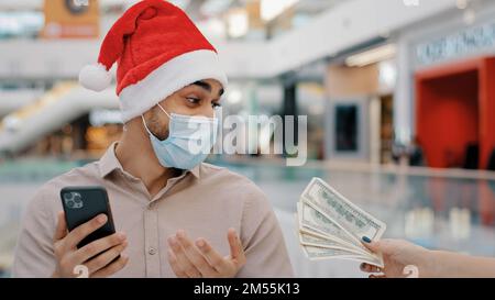 Ethnischer Mann männlich in medizinische Maske in Weihnachten Weihnachten Weihnachtsmann Hut Wetten mit Handy Casino Wette Online Bank Zahlung Kreditservice schnelles Geld Stockfoto