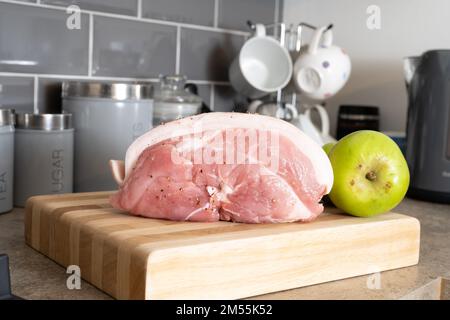 Rohes, ungekochtes Schweinebein mit Apfel auf einem Holzbrett Stockfoto