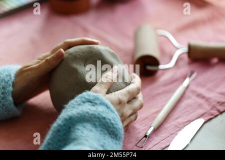 Weibliche Töpferkünstlerin bereitet Ton zum Formen vor. Nahaufnahme von Frauenhänden mit Ton. Kreative Handarbeit. Keramikstudio. Stockfoto