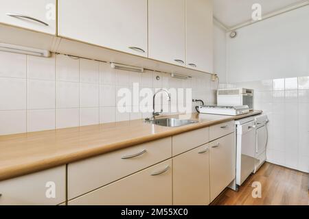 Eine Küche mit Holzablageflächen und weißen Schränken in der Rückwand, es gibt eine Spülmaschine neben dem Waschbecken Stockfoto