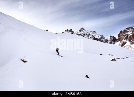 Skifahrer mit rotem Rucksack im Helm und Maske in den schneebedeckten Bergen. Sport im Freien in der Wintersaison. Stockfoto