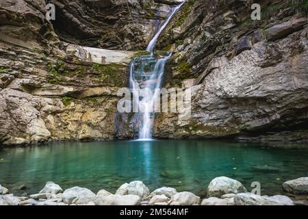 Wunderbarer kleiner Wasserfall, der einen smaragdgrünen Teich in einem Herbstwald bildet Stockfoto