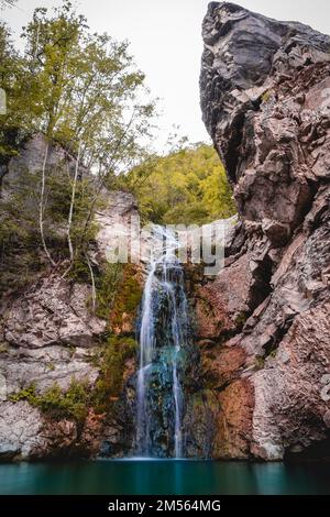Wunderbarer kleiner Wasserfall, der einen smaragdgrünen Teich in einem Herbstwald bildet Stockfoto