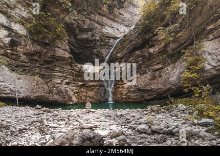 Wunderbarer kleiner Wasserfall, der einen smaragdgrünen Teich in einem Herbstwald bildet Stockfoto