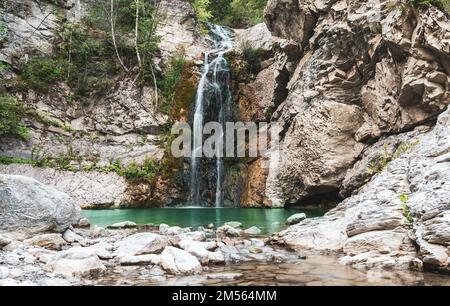 Wunderbarer kleiner Wasserfall, der einen smaragdgrünen Teich in einem Herbstwald bildet Stockfoto