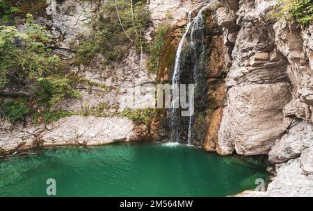 Wunderbarer kleiner Wasserfall, der einen smaragdgrünen Teich in einem Herbstwald bildet Stockfoto
