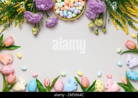 Osterkomposition. Von oben sichtbarer Rahmen mit Eiern in Korb, lila, gelben Blumen auf grauem Hintergrund Stockfoto
