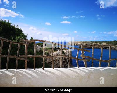 Ein Strand in Binibeca (Menorca), der durch ein Holzgeländer eines Balkons gesehen wird Stockfoto