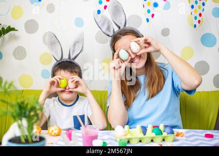 Mutter und ihr Sohn halten farbenfrohe Ostereier vor den Augen Stockfoto