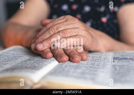 Eine alte Frau liest die Bibel, die Hände sind dicht. Stockfoto