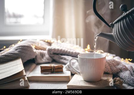 Gemütliche Komposition mit einer Teekanne, einer Tasse und einem Buch auf verschwommenem Hintergrund. Stockfoto