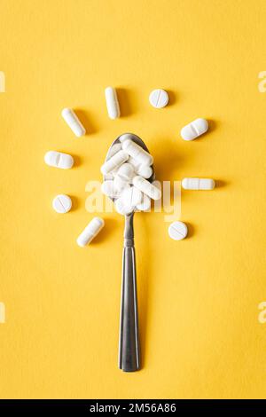 Weiße Pillen in Löffel in Form einer Blume auf gelbem Hintergrund, flach liegend. Stockfoto