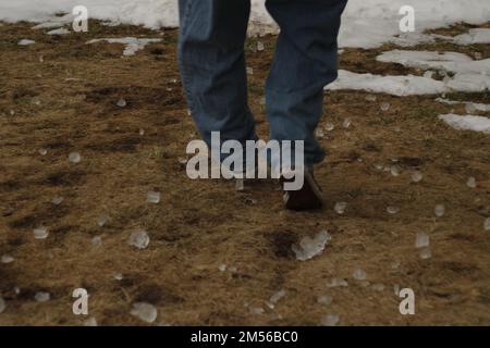 Eine Rückansicht der Füße eines Mannes, der mit einem großen Stück Graupel auf dem Boden läuft Stockfoto