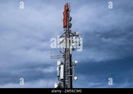 Geringer Blickwinkel auf einen Kommunikationsturm mit Antennen und Sendern gegen bewölkten Himmel. Kommunikationstechnologie und Telekommunikationsindustrie. Stockfoto