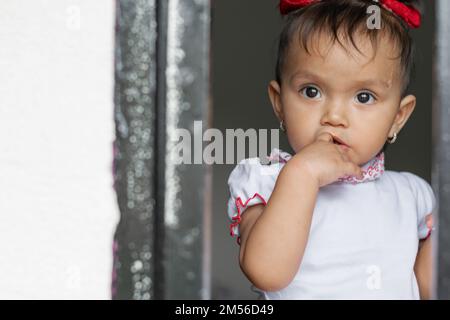 Dunkelhaariges Baby, schaute aus dem Fenster, ein Finger steckte in ihrem Mund. Stockfoto