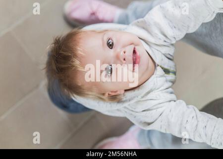 Das hübsche Baby lehnte sich zurück und hielt moms Hände Stockfoto