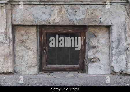 Kleines schäbiges Kellerfenster in einem Steingebäude Stockfoto