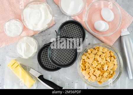 Käsekuchen-Rezept. Drei kleine runde Kuchenpfannen (Dose, Schimmel) und frische Zutaten für das Käsekuchen-Rezept, Nahaufnahme auf dem Küchentisch, flach liegend Stockfoto