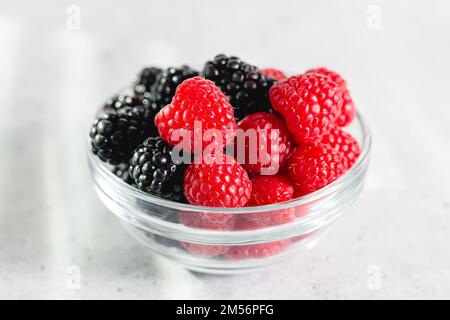 Frische reife Himbeeren und Brombeeren in einer Glasschüssel auf dem Küchentisch Stockfoto