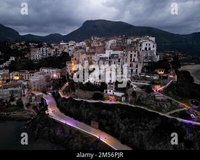 Eine Luftaufnahme über Sperlonga Stadt, beleuchtet am Abend unter dem Wolkenhimmel, Italien Stockfoto