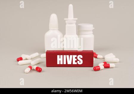Medizinisches Konzept. Auf einer grauen Oberfläche sind Pillen, weiße Gläser und ein roter Holzblock mit der Inschrift - Bienenstöcke Stockfoto