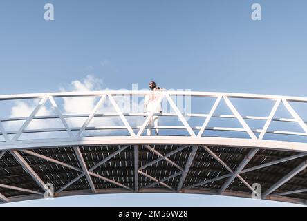 Ein kleiner Winkel von einer glatzköpfigen afroamerikanischen Führungskraft, die mono-chromatisch gekleidet ist, in einem weißen Anzug mit einem gut gepflegten Bart, auf dem ihr Arm ruht Stockfoto