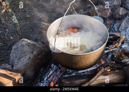 Kessel mit kochender Touristensuppe hängt über einem offenen Feuer, Campingmahlzeit Stockfoto