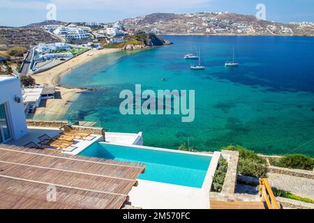 Wunderschöne Aussicht auf die Bucht auf der griechischen Insel Mykonos mit mehreren Segelbooten (Yachten). Im Vordergrund befindet sich ein typischer blauer Wasserpool Stockfoto