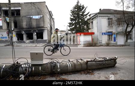 IZIUM, UKRAINE - 25. DEZEMBER 2022 - Ein älterer Mann fährt an einer Straße vorbei, die von der Beschuss russischer Truppen in Izium betroffen ist, die aus Russland befreit wurden Stockfoto