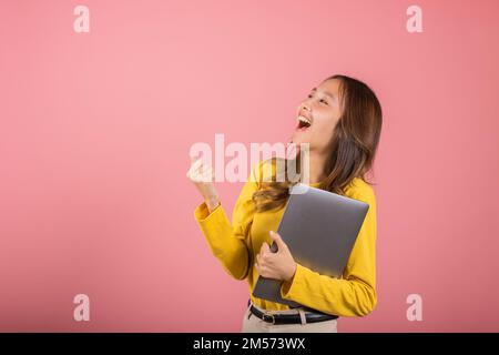 Selbstbewusste Frau, die ein lächelndes Gesicht hält und einen Laptop hält, hebt die Hand und sagt Ja Stockfoto