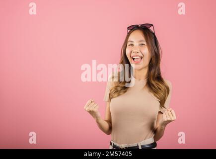 Eine junge Frau, die eine Brille trägt, hebt die Hand hoch und feiert ihre erfolgreiche Geste Stockfoto