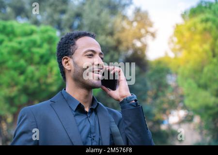 Nahaufnahme eines attraktiven jungen afroamerikanischen Mannes, der im Freien mit einem Mobiltelefon spricht Stockfoto