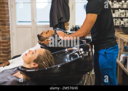 Ein paar Besuche im Schönheitssalon. Zwei Personen, die Shampoo-Stühle in einem Friseursalon benutzen. Unbekannte Friseurin wäscht Haare von zwei Klienten. Hochwertiges Foto Stockfoto