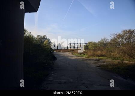 Unbefestigter Pfad mit Pfützen und einer Brücke im Hintergrund auf dem Land Stockfoto
