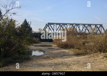 Unbefestigter Pfad mit Pfützen und einer Brücke im Hintergrund auf dem Land Stockfoto